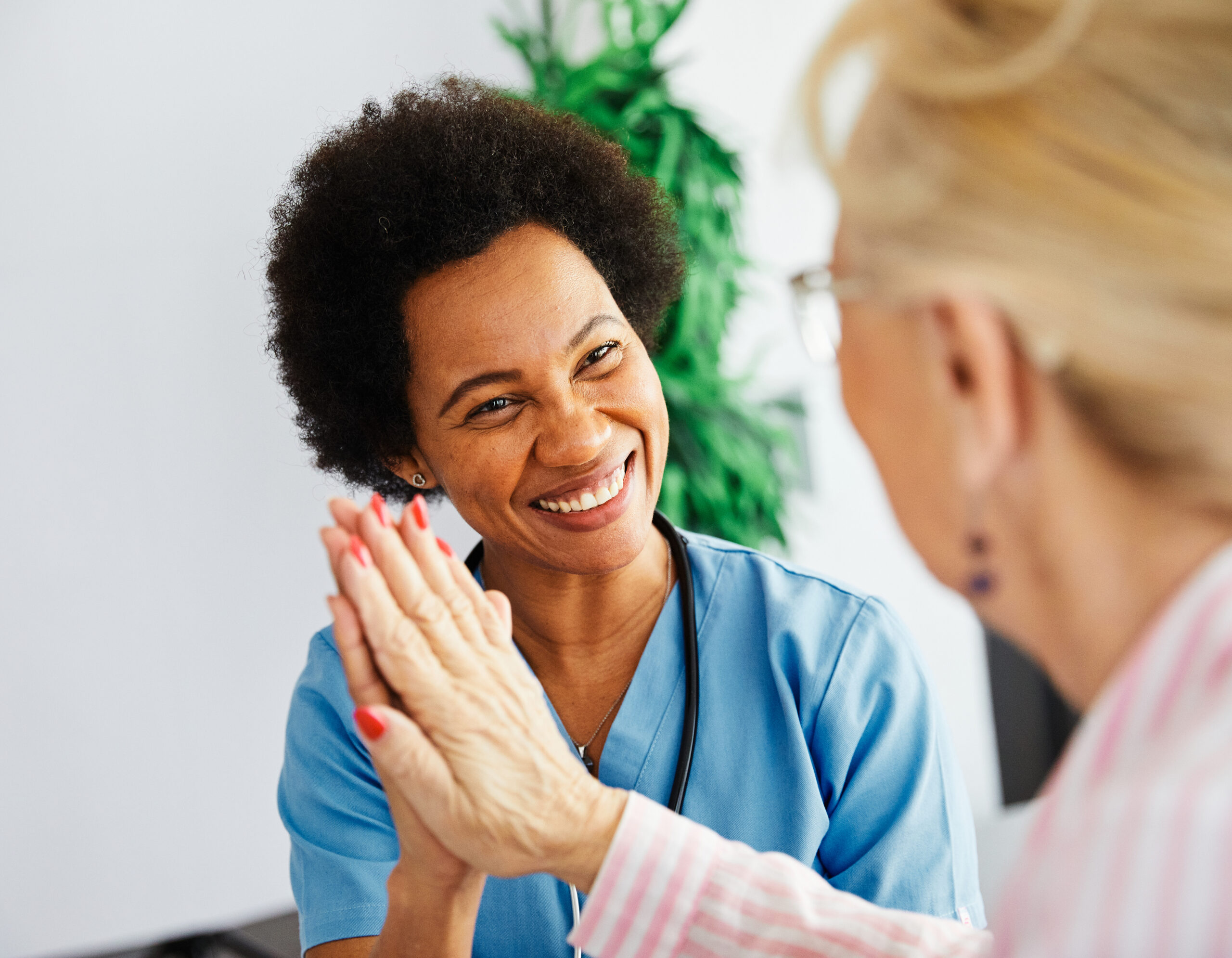 Smiling female caregiver in blue scrubs giving a high-five to a senior woman, symbolizing trust, encouragement, and quality home care assistance.