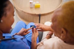 Nurse assisting elderly woman with blood sugar monitoring device.