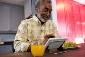 Smiling senior man using a tablet at home, symbolizing how smart devices help older adults stay connected and manage daily routines independently.