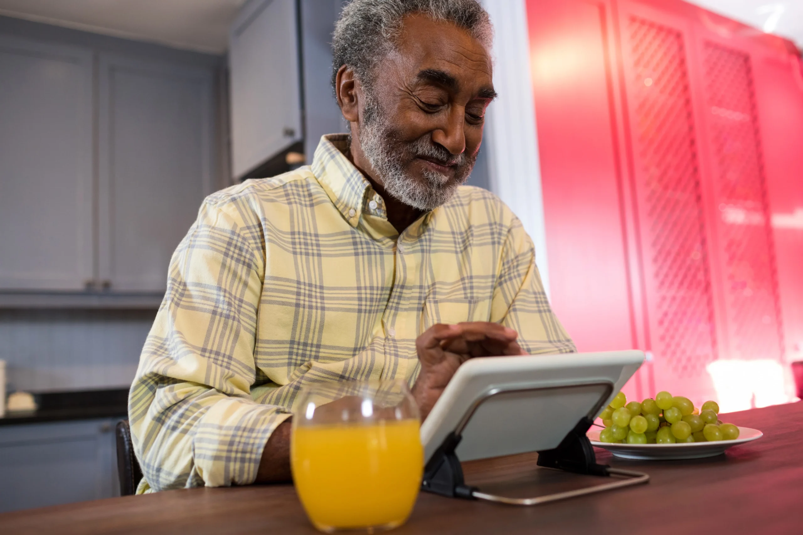 Smiling senior man using a tablet at home, symbolizing how smart devices help older adults stay connected and manage daily routines independently.